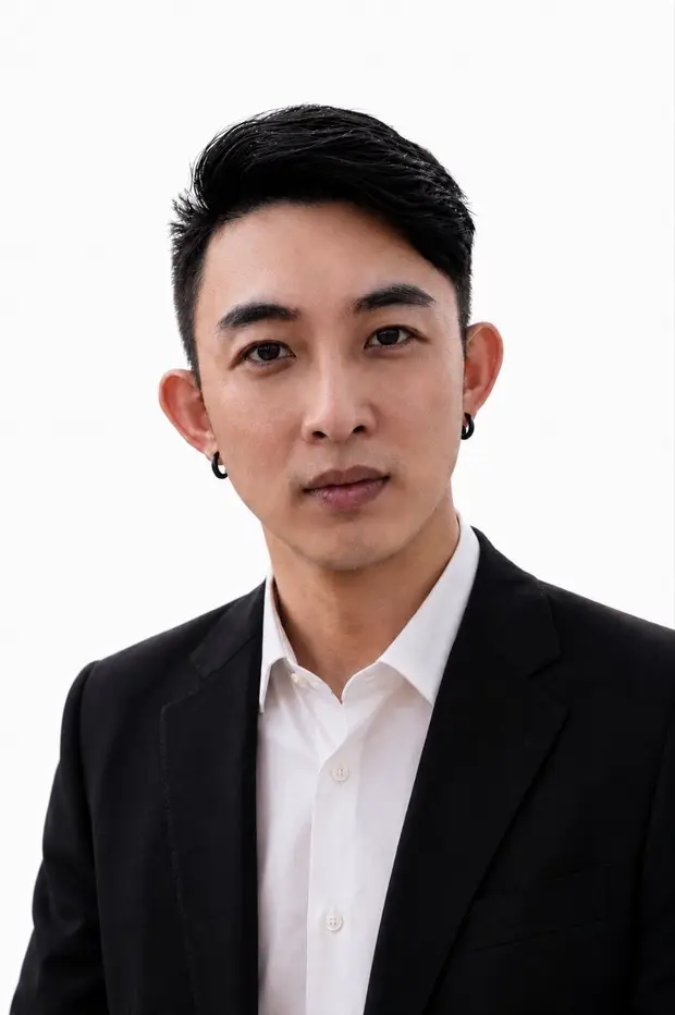 A man in a black suit and white shirt looks directly at the camera against a white background.